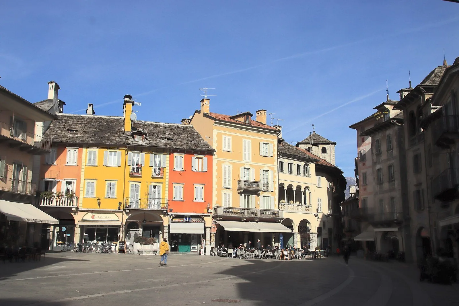 Piazza Mercato a Domodossola in una giornata di sole, con le case colorate, i tetti in pietra e i portici sul lato della piazza